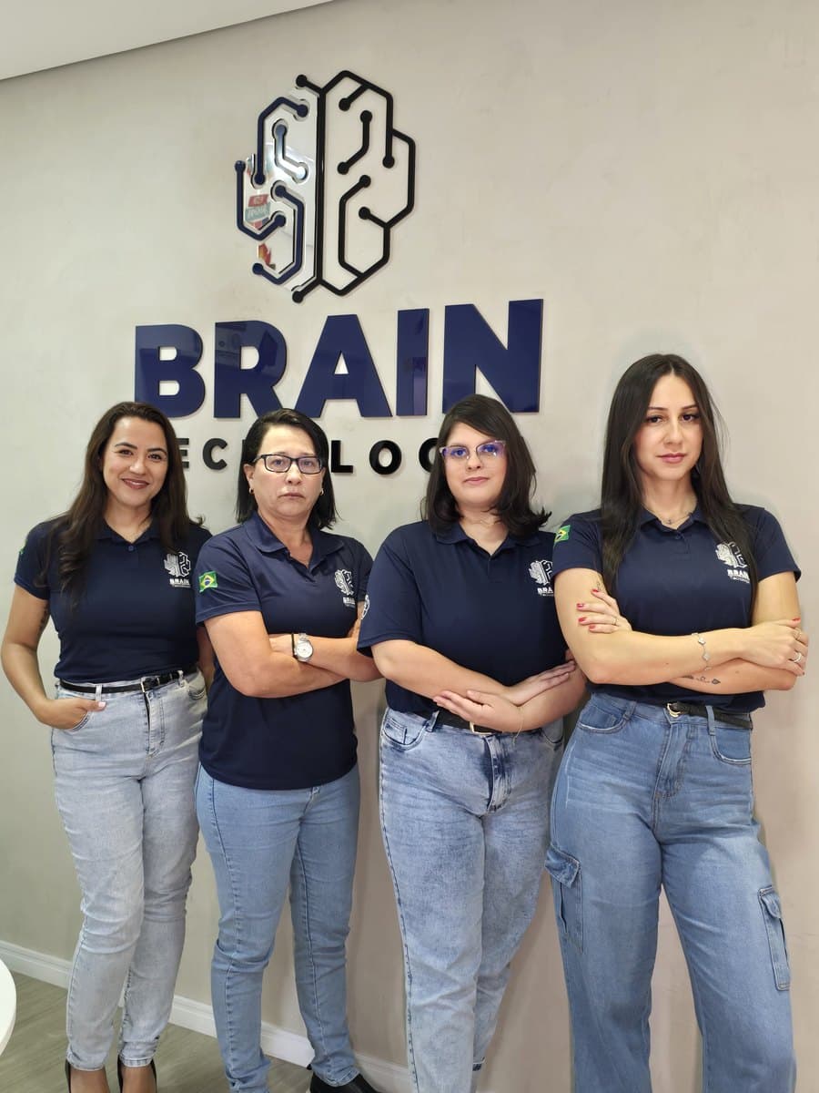 Quatro colaboradoras da Brain de uniforme em frente à parede com a marca