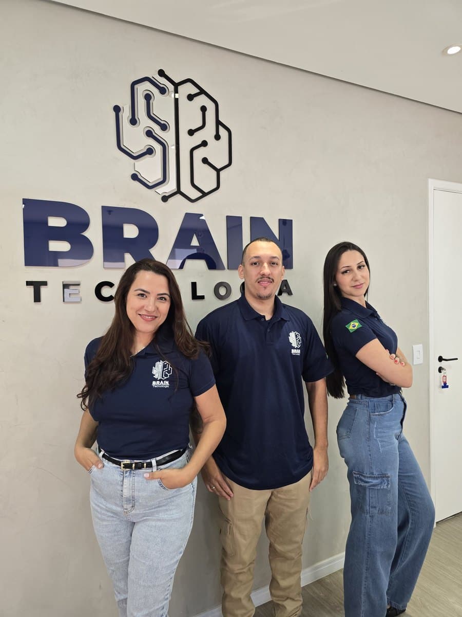 Trio de colaboradores da Brain de uniforme em frente à parede com a marca