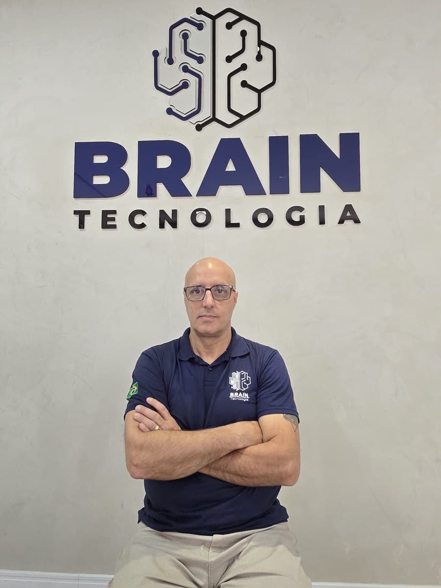 Colaborador da Brain de uniforme em frente à parede com a marca